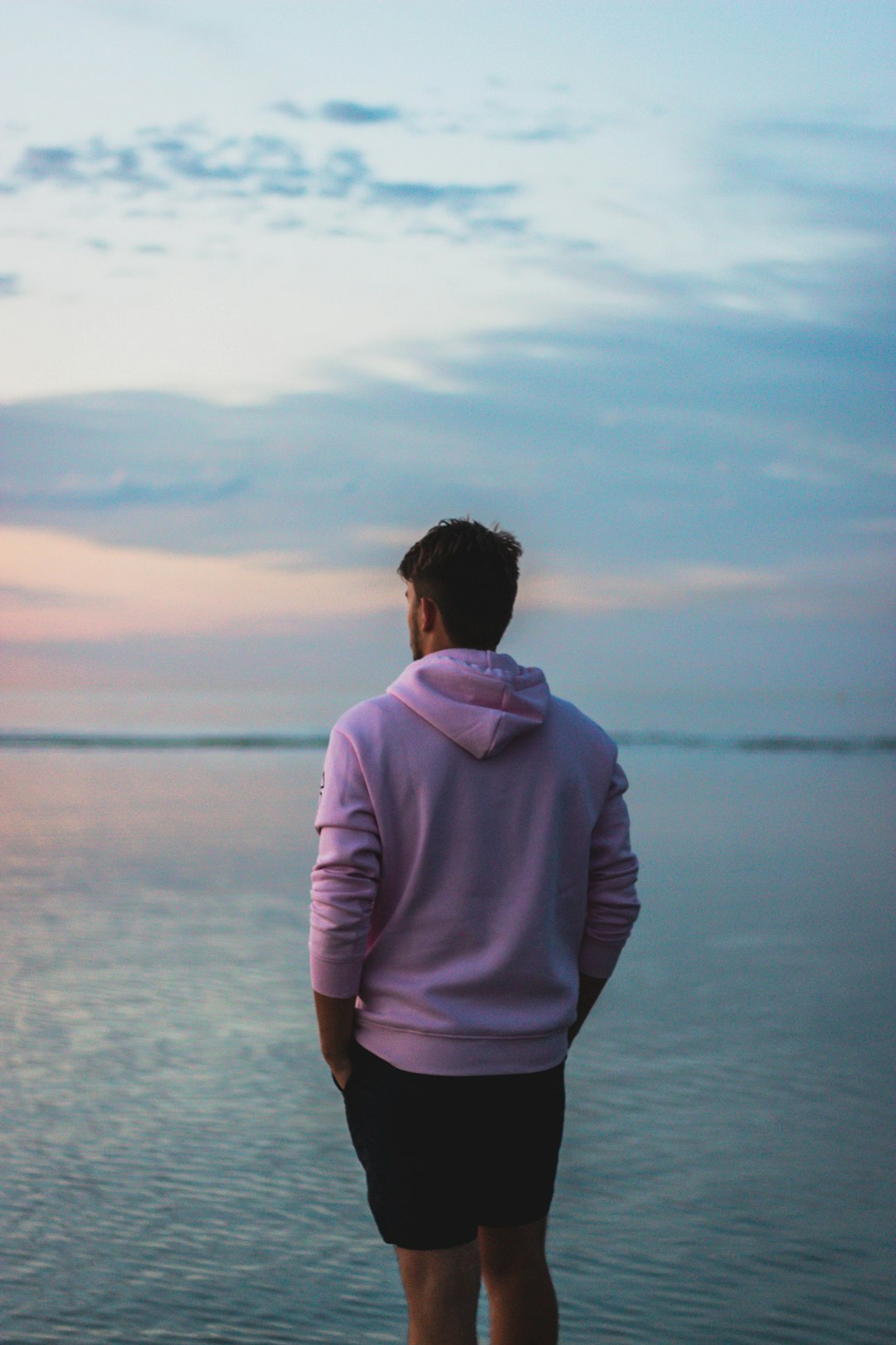 man in purple hoodie standing on seashore during daytime
