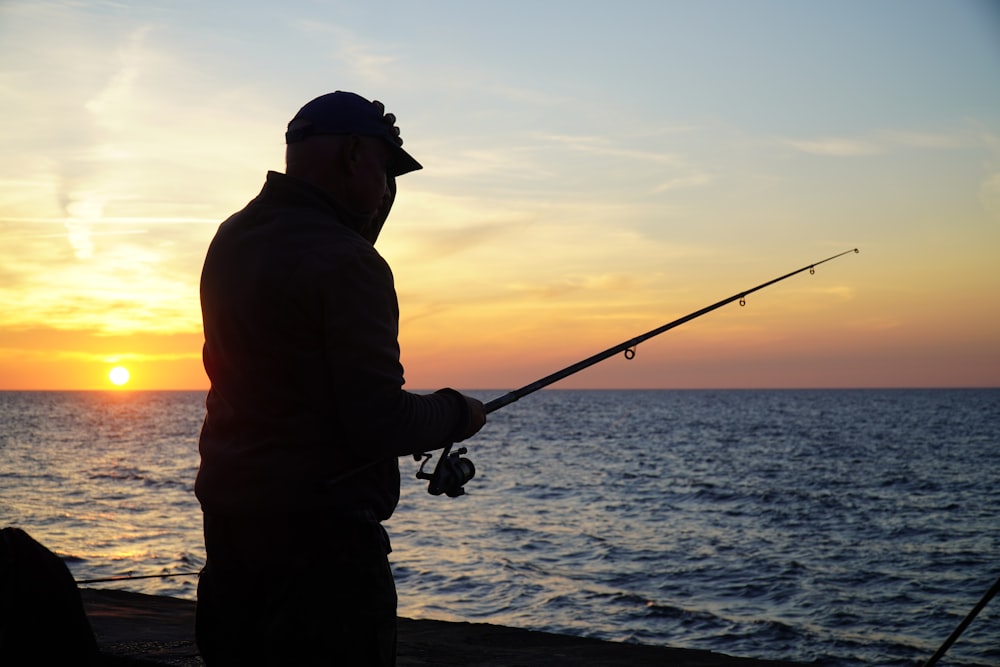 silhouette of man fishing on sea during sunset