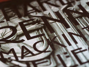 A close-up view of a section of a stone or metal engraving featuring large, bold letters intertwined with classical architectural elements. The surface appears textured, adding depth and contrast.