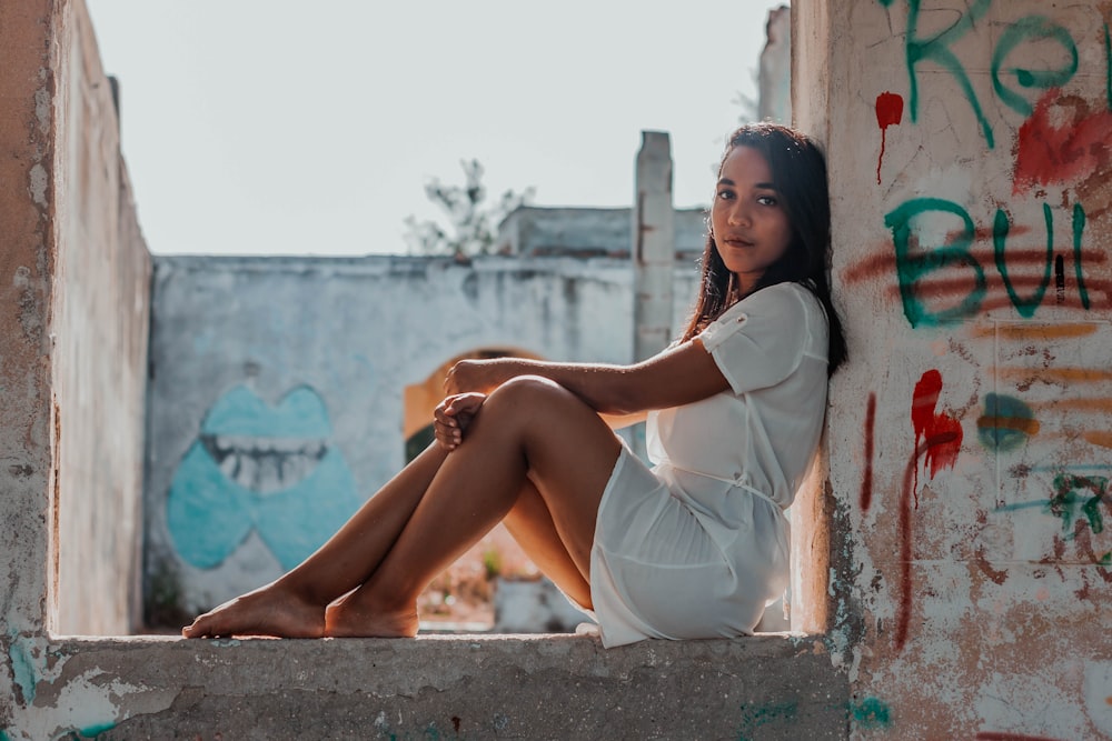 woman in white dress sitting on concrete wall during daytime