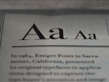 The image displays a close-up of text on a page, showcasing different styles and weights of the letter 'A'. Below the large 'A' letters, there is more printed text in a serif font, detailing historical information about Emigre Fonts in Sacramento, California.
