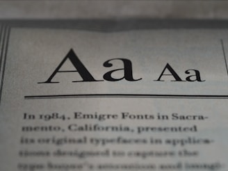 The image displays a close-up of text on a page, showcasing different styles and weights of the letter 'A'. Below the large 'A' letters, there is more printed text in a serif font, detailing historical information about Emigre Fonts in Sacramento, California.