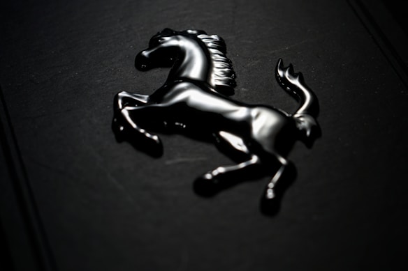 A shiny, black prancing horse emblem is mounted on a dark background. The lighting highlights the sleek contours and details of the horse, giving it a dynamic and luxurious appearance.