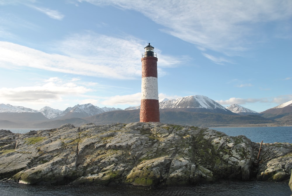 昼間の青空の下で灰色の岩層に浮かぶ赤と白の灯台