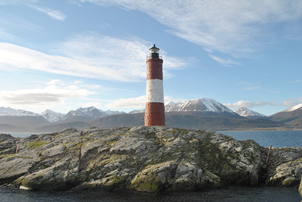 Phare rouge et blanc sur une formation rocheuse grise sous un ciel bleu pendant la journée