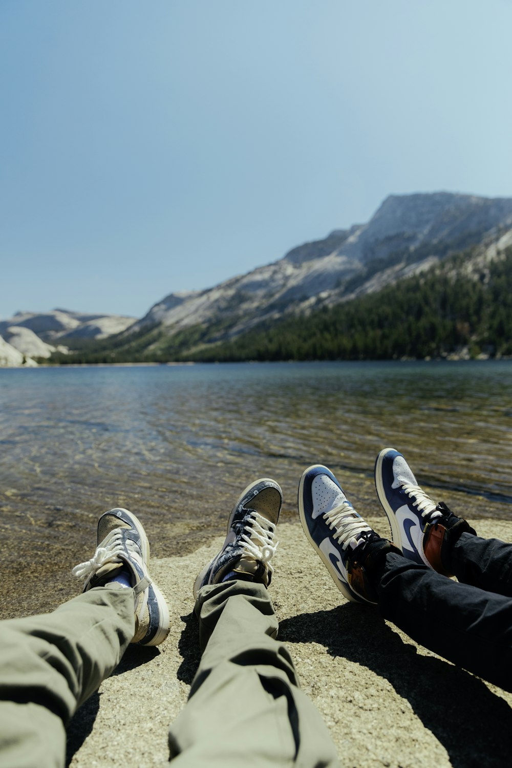 person in black pants and white sneakers sitting on rock near body of water during daytime