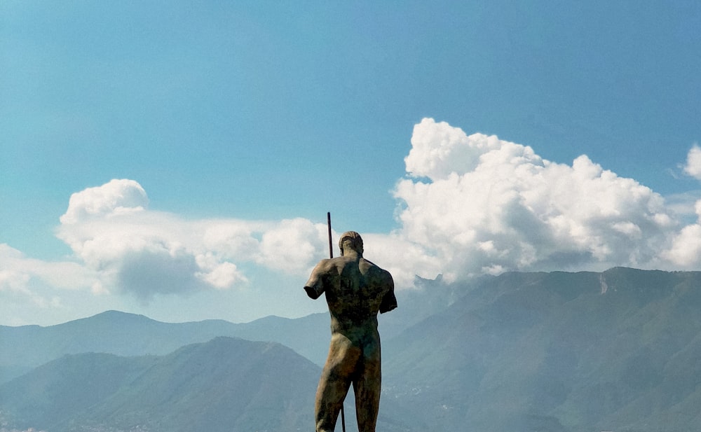 man in green and black camouflage jacket holding rifle standing on rock formation under blue sky