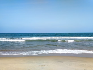 A serene beach scene with gentle waves lapping at the shore under a clear blue sky.