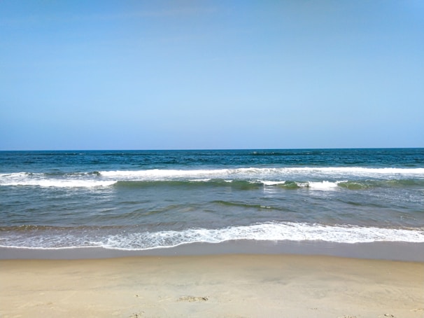 A serene beach scene with gentle waves lapping at the shore under a clear blue sky.
