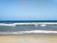 A serene beach view with gentle waves lapping against the shore under a clear blue sky.