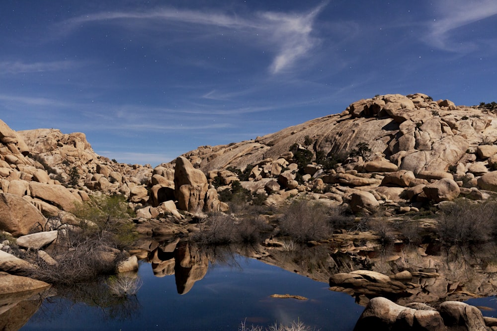 brown rocky mountain beside blue lake under blue sky during daytime