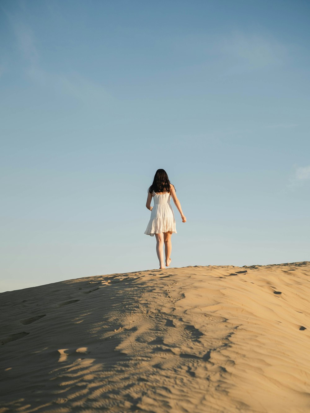 femme en robe blanche debout sur le sable brun pendant la journée