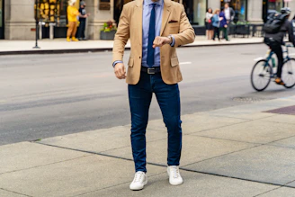 person in blue denim jeans and brown coat standing on sidewalk during daytime