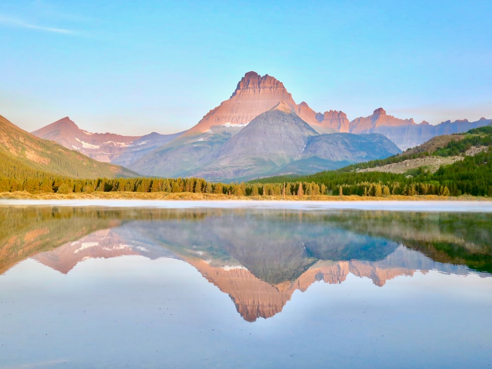 lake near green grass field and mountain under blue sky during daytime