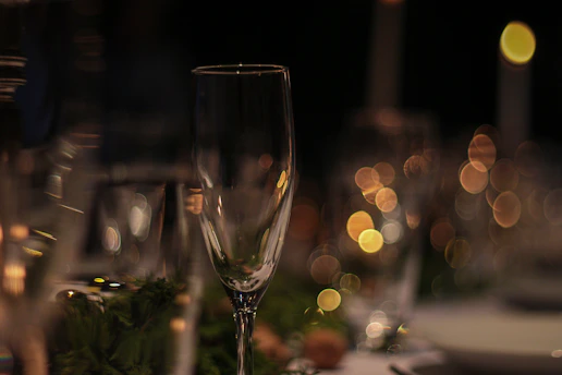 A close-up of a delicate champagne flute catching the soft glow of golden light, set against a minimalist off-white background.