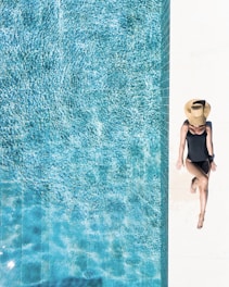 woman in black bikini bottom and white sun hat standing on blue water