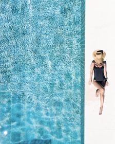 woman in black bikini bottom and white sun hat standing on blue water