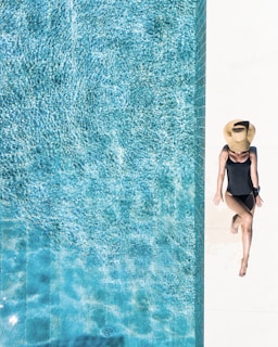 woman in black bikini bottom and white sun hat standing on blue water
