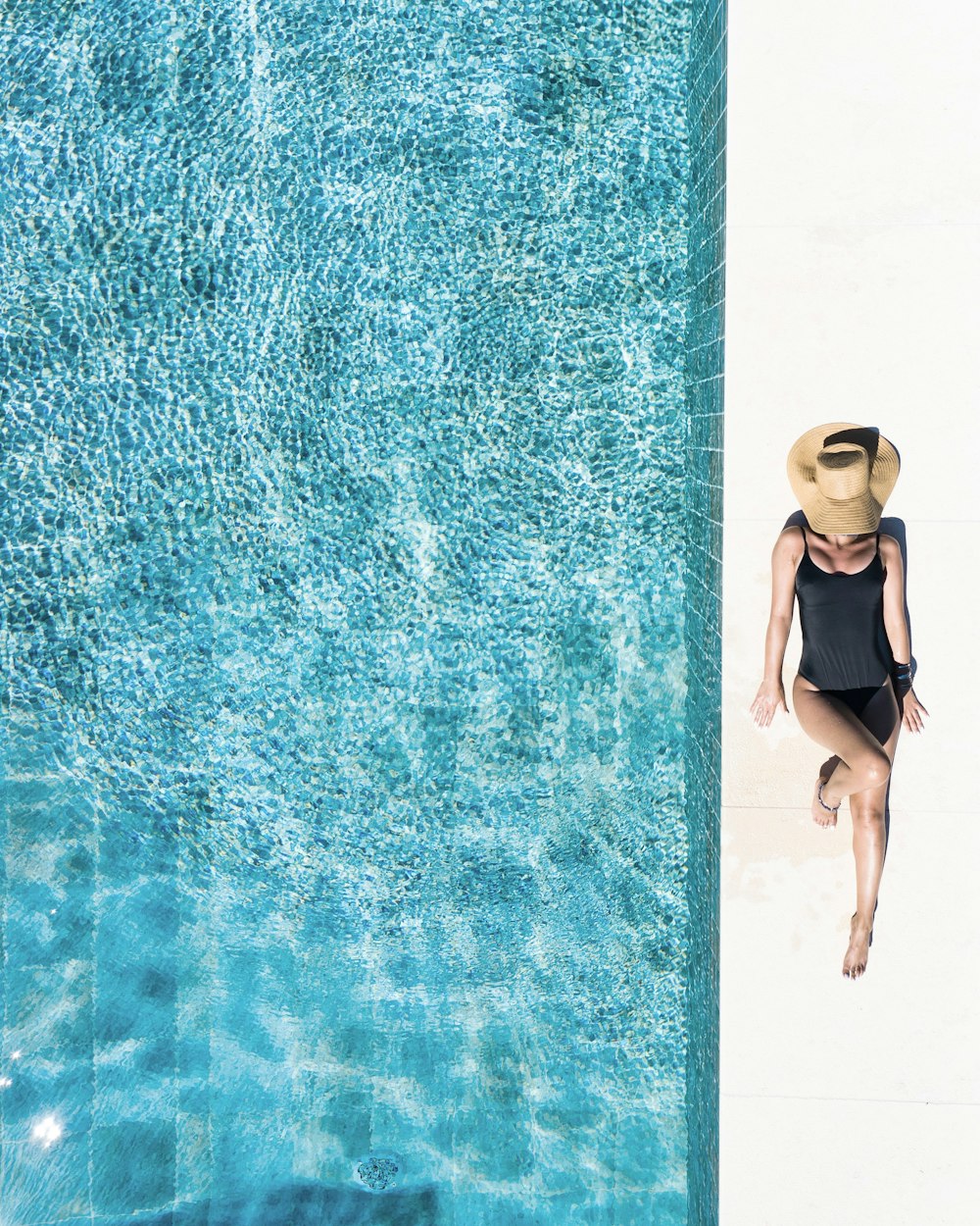 mujer en la parte inferior del bikini negro y sombrero blanco para el sol de pie sobre el agua azul