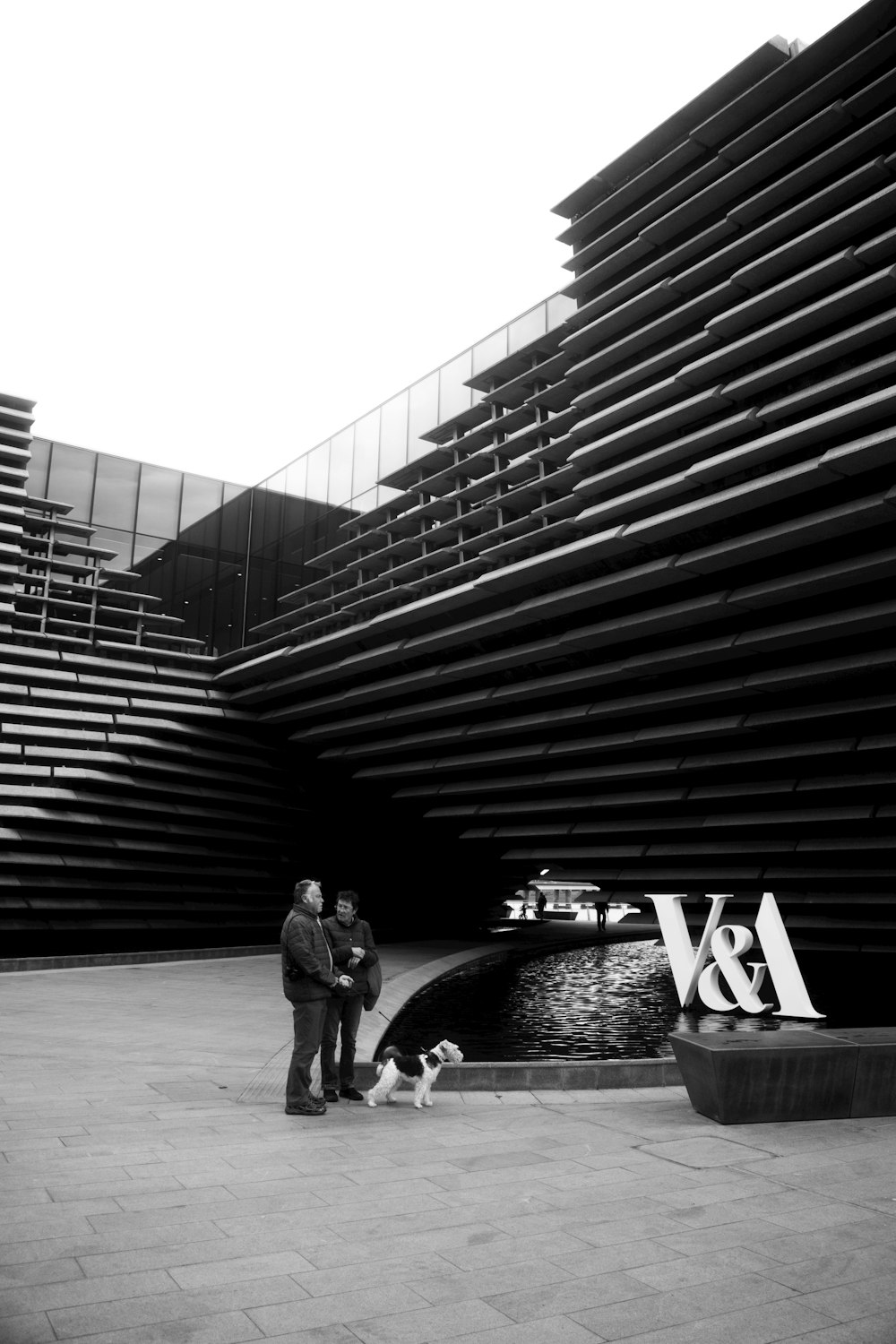 grayscale photo of man and woman walking on sidewalk