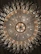 An ornate chandelier with intricate crystal and gold detailing hangs from the ceiling, radiating light. The symmetrical design includes numerous crystal elements that create an elegant and luxurious appearance.