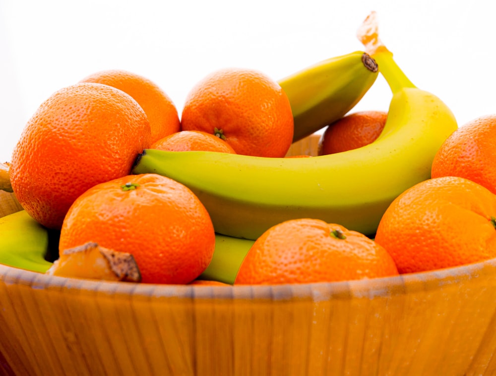 Fruta de naranja y plátano en canasta tejida marrón