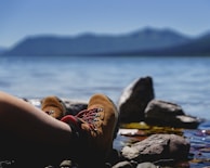 A close-up of well-worn hiking boots resting beside a crystal-clear mountain lake.