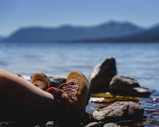 A close-up of well-worn hiking boots resting beside a crystal-clear mountain lake.