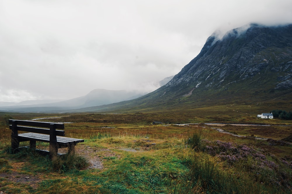 brown wooden bench on green grass field near mountain under white clouds during daytime