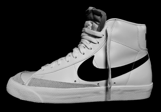 A white high-top sneaker with a prominent black swoosh logo on the side. The shoe features white laces and a textured rubber sole. The tongue and collar of the sneaker are also visible.
