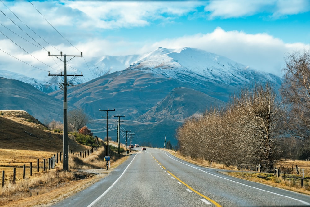 gray concrete road near brown trees and mountain under blue sky during daytime