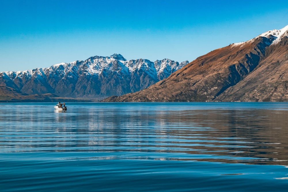 2 people riding on boat on lake near snow covered mountain during daytime