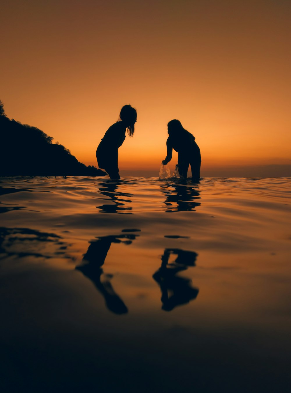 silhouette of 2 person standing on seashore during sunset