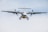 A twin-engine turboprop aircraft is captured in flight, viewed from the front. The propellers are spinning, and the landing gear is extended. The sky behind the airplane is clear with a light blue hue.