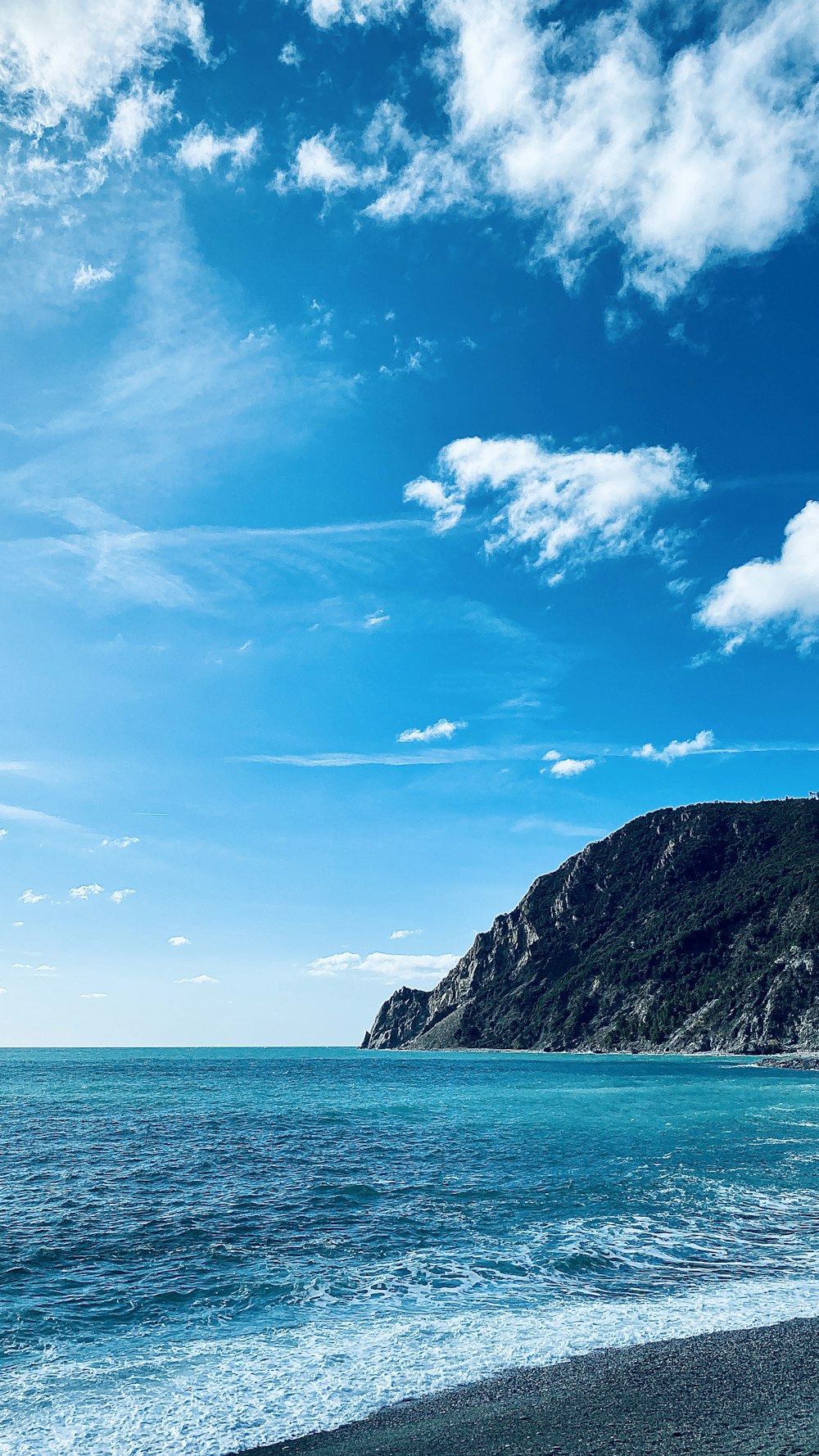 blue sea beside green mountain under blue sky during daytime