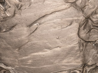 Swirling and smoothed texture of a muddy or clay-like substance, featuring a range of brown shades with some lighter streaks. The surface appears wet, with wavy patterns that suggest movement or layering of the material.