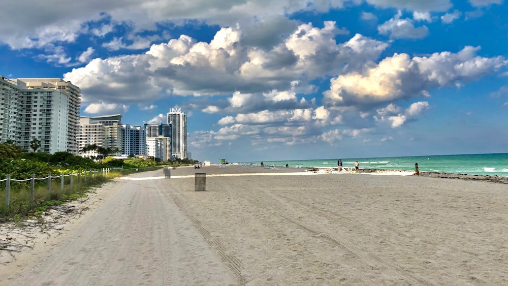 white sand beach near city buildings under blue and white sunny cloudy sky during daytime