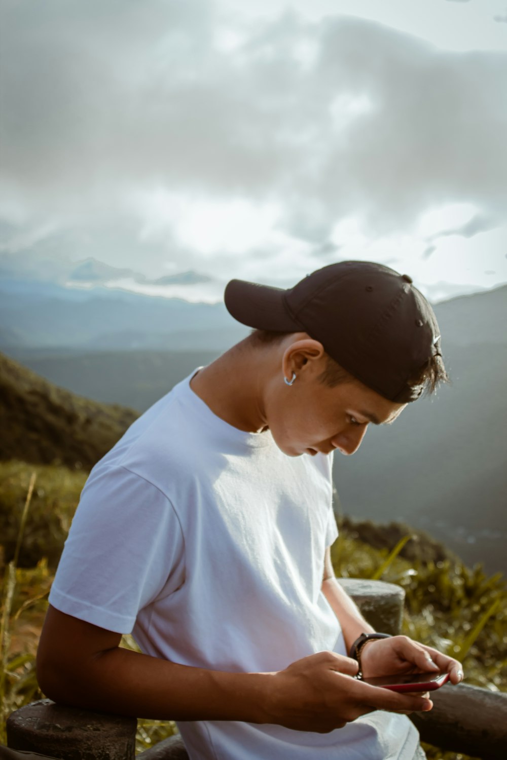 man in pink crew neck t-shirt and black cap sitting on rock during daytime