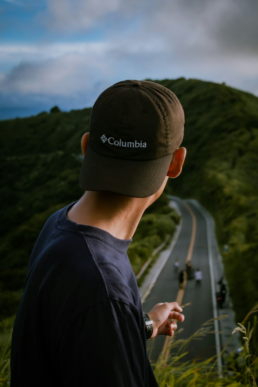 man in black crew neck shirt wearing black cap standing on road during daytime