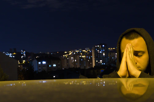 Neon-lit silhouettes of a small group praying on a city rooftop at dusk.