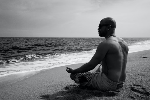 topless man in shorts sitting on beach shore