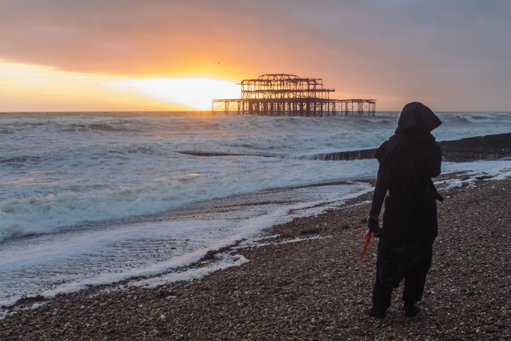 silhouette of man standing on seashore during sunset