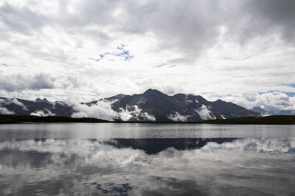 snow covered mountain near body of water under cloudy sky during daytime