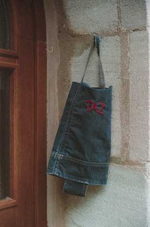 Tote bag with elcambiodeguardia logo hanging on a rustic door handle.