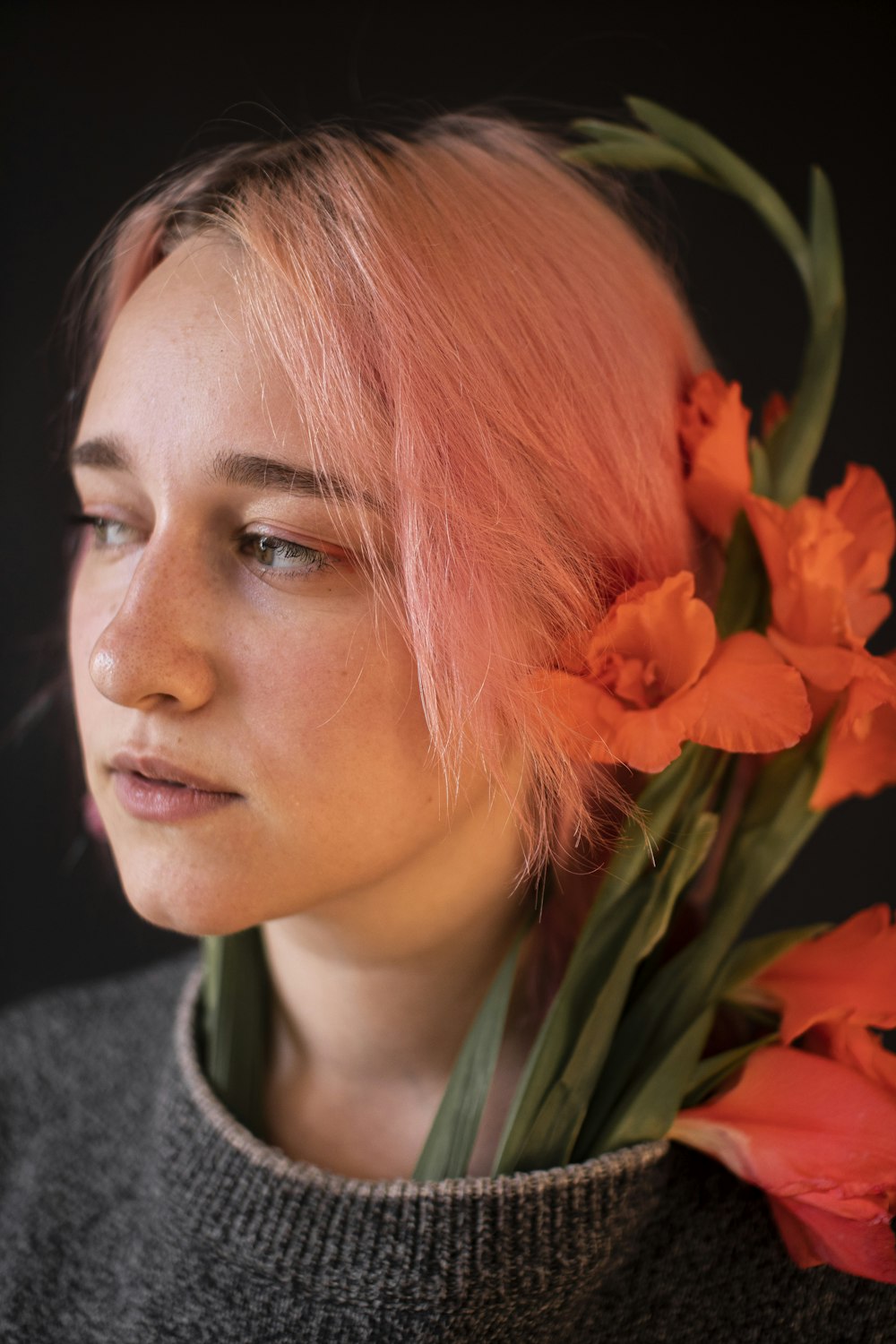 woman in gray hoodie standing beside red flower