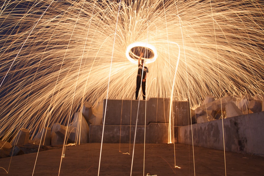 man standing on gray concrete wall with steel wool during night time