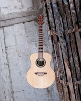 Close-up of a vintage acoustic guitar resting against a wooden wall.