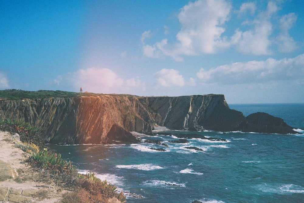 brown and green mountain beside body of water under blue sky during daytime