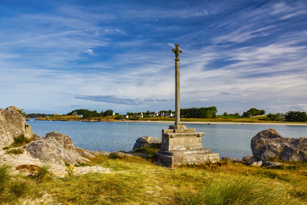 gray concrete cross on gray rock near body of water under blue sky during daytime