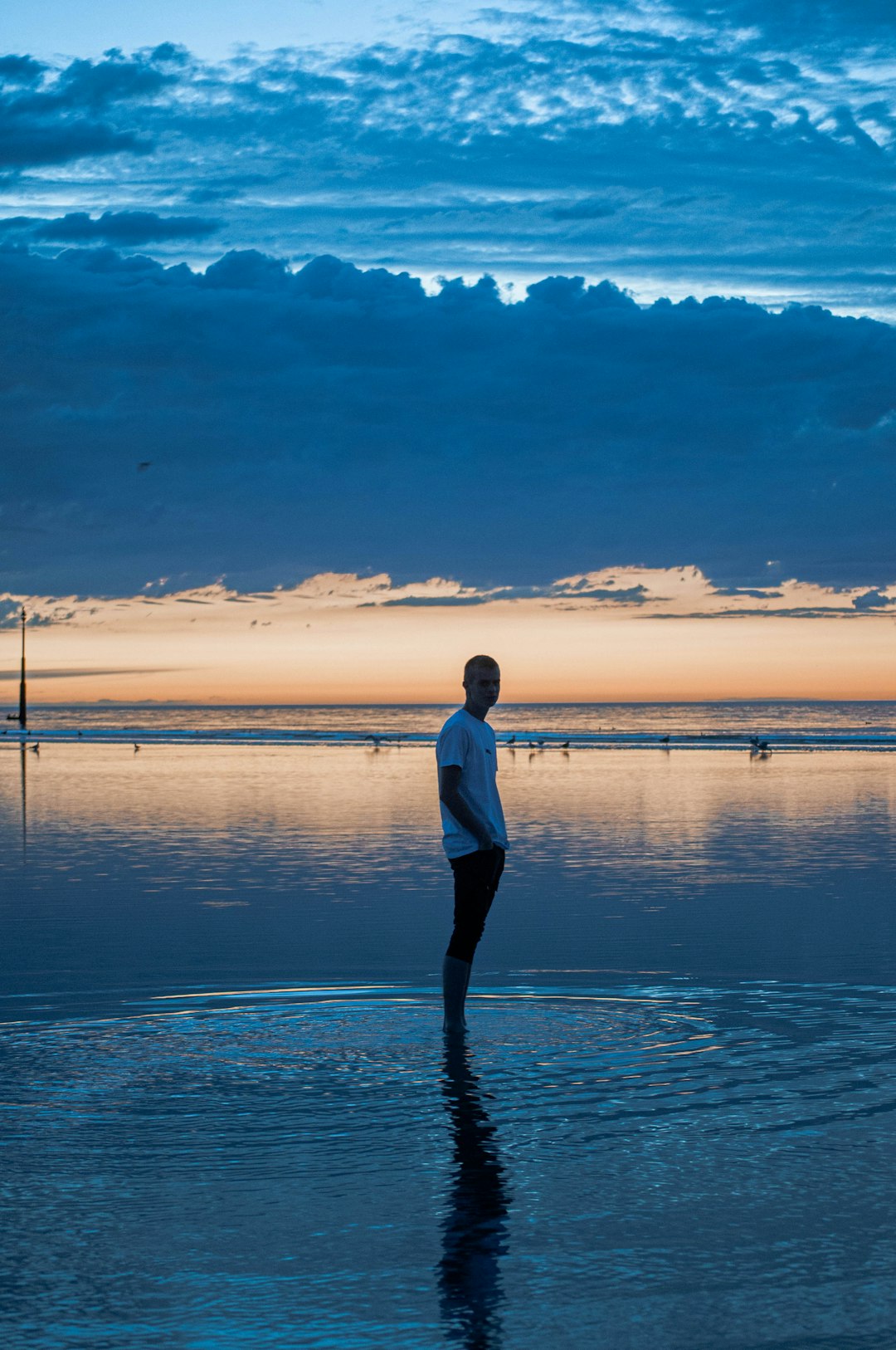 woman in white long sleeve shirt and black pants standing on seashore during sunset